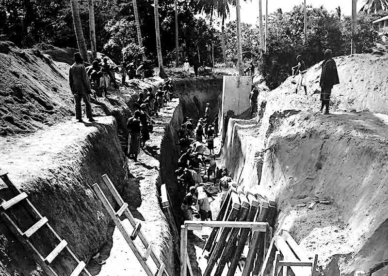 Des indigènes creusent des tranchées sous la supervision de soldats et d'un askari.